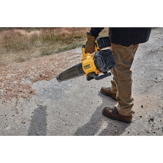 Person using a DEWALT cordless leaf blower to clear debris from a paved outdoor surface.