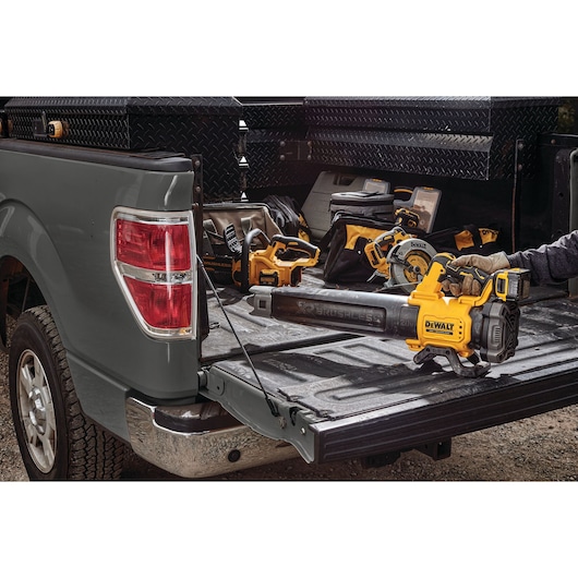 A DEWALT cordless leaf blower and other power tools are displayed on the open bed of a grey pickup truck, with various toolboxes and bags in the background.