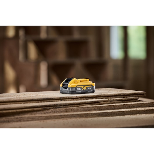 A DEWALT 20V XR 5Ah battery resting on a stack of wooden boards in a workshop setting.