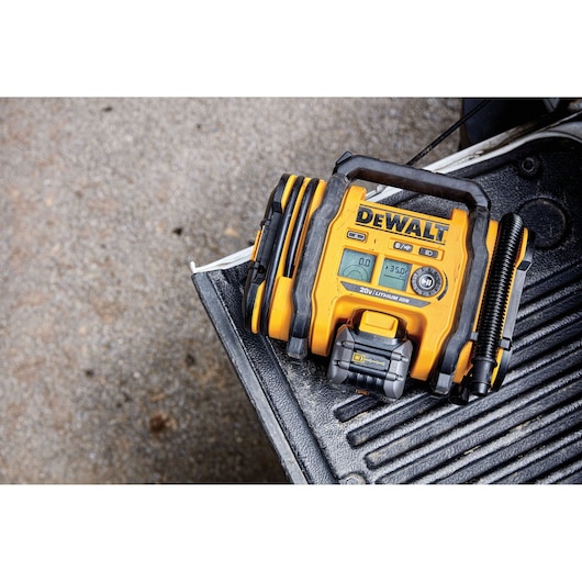 A DEWALT 20V Lithium Ion portable air inflator with a digital display and hose, placed on the back of a truck bed.