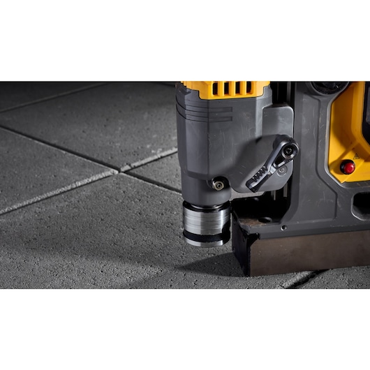 Close-up of a DEWALT power tool positioned on concrete tiles, highlighting the drill attachment and part of the tool's body.