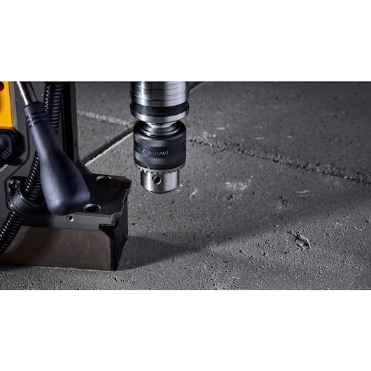 Close-up of a DEWALT magnetic drill press, focusing on the drill bit and base positioned over a concrete surface.