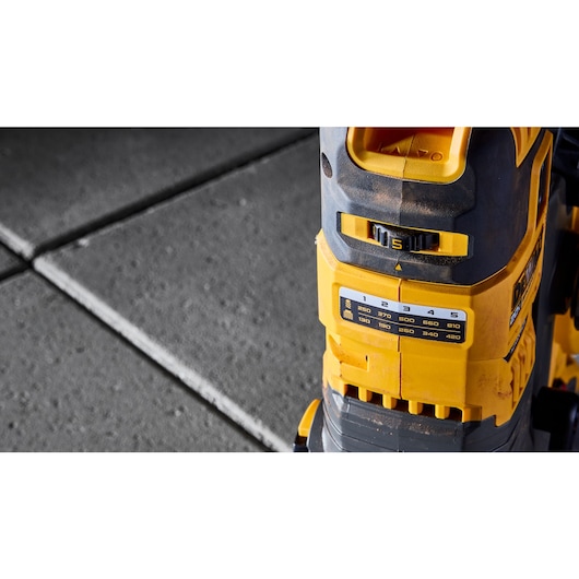 Close-up of a yellow and black DEWALT power tool with adjustable settings, placed on a concrete surface.