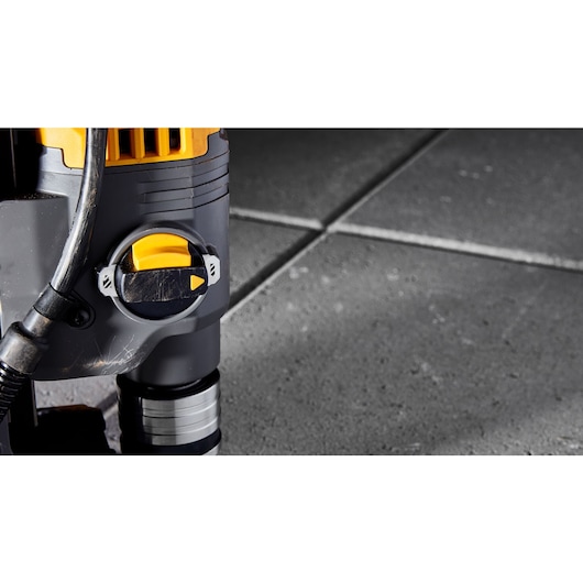 Close-up view of a DEWALT power tool with a yellow and black adjustment knob, placed on grey tiled flooring.