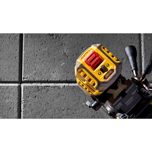 Close-up view of a DEWALT power tool with a yellow and black casing and a red switch, placed on a gray textured surface with square tile patterns.