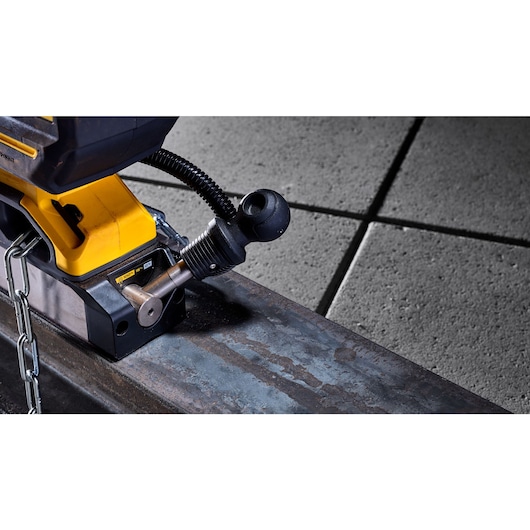 Close-up of a DEWALT cordless magnetic drill press, model DCD1623B, secured to a metal beam with a chain. The focus is on the control area and mounting mechanism.