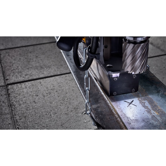 Close-up of a DEWALT magnetic drill being used on a metal beam, with a chain attached and a marked spot for drilling.