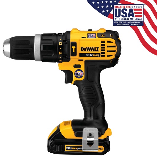 A yellow and black DEWALT 20V MAX cordless drill with multiple USA flag stickers indicating it is made in the USA with global materials. The drill has a keyless chuck and a visible battery at the base. Part of an American flag with product labeling is shown in the top right corner.