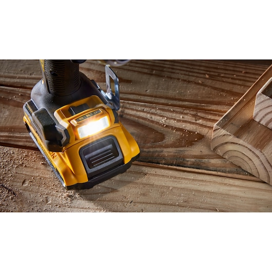 Close-up of the base and LED light of a yellow and black DEWALT cordless power drill placed on a wooden surface with sawdust.