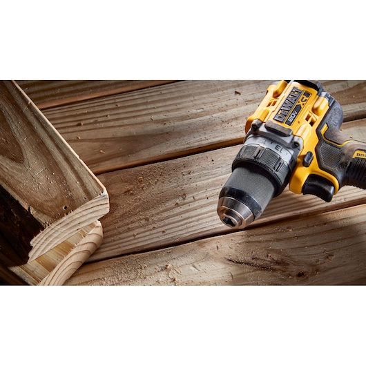 A close-up view of a DEWALT 20V cordless drill shown on a wooden work surface next to cut wooden boards, with wood shavings scattered around.