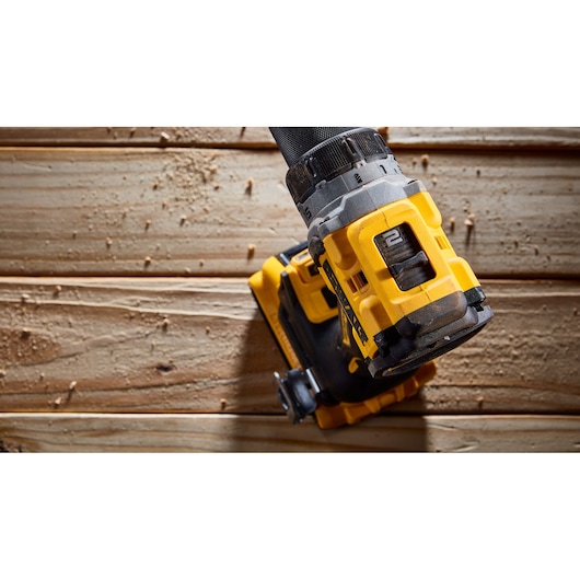 Close-up view of a DEWALT cordless drill being used on a wooden surface with wood shavings around.