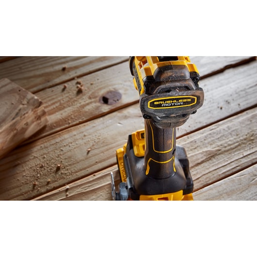 A close-up view of a DEWALT cordless power drill with a brushless motor, placed on a wooden surface with wood shavings around.