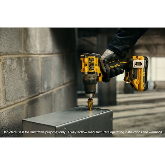 A close-up of a gloved hand using a DEWALT cordless drill to drill into a metal surface in an industrial environment.