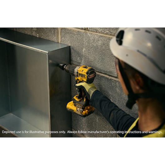 A person wearing a helmet and gloves is using a yellow and black DEWALT cordless drill to drill into a metal surface mounted against a concrete wall.