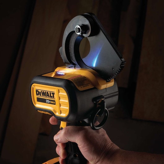 A close-up view of a DEWALT 20V MAX cordless cable cutter, being held in someone's hand. The tool features a large cutting head designed for cutting thick cables.
