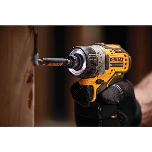 A close-up of a gloved hand using a DEWALT 12V MAX cordless drill to drive a screw into a piece of wood.