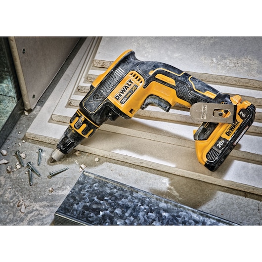 A DEWALT DCF620D2 cordless drywall screwgun placed on a construction surface, surrounded by screws and building materials.