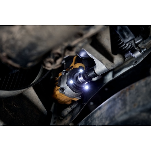 A close-up view of a DEWALT cordless impact wrench being used on a mechanical part under a vehicle. The tool features bright LED lights illuminating the work area.