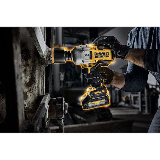 A close-up of a person using a DEWALT 20V XR cordless impact wrench on a large metal bolt in an industrial setting. The tool is highlighted with a glowing outline, and the person is wearing gloves.