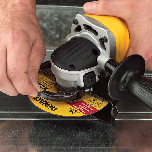 Close-up of a person adjusting a DEWALT angle grinder with a yellow abrasive disc, preparing it for use on a metal surface.