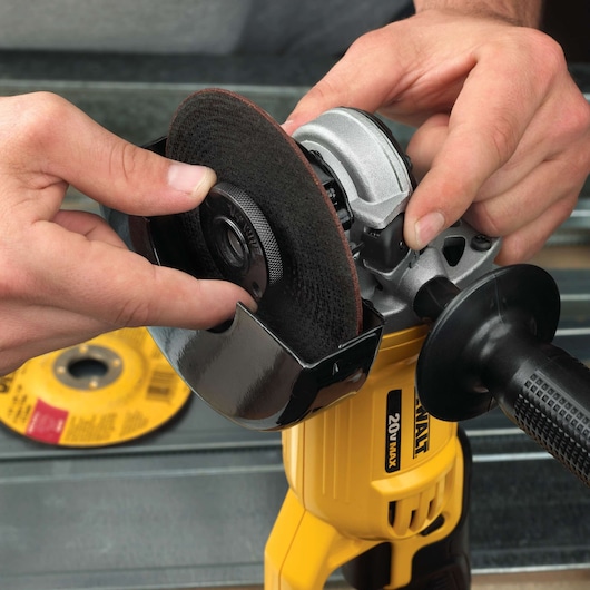 A close-up view of hands installing a grinding disc onto a yellow DEWALT 20V Max angle grinder.