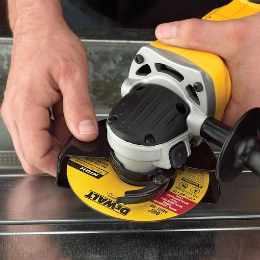 Close-up of hands using a DEWALT angle grinder with a yellow grinding disc on a metal surface.