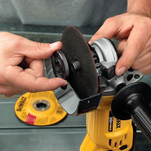 A close-up of hands attaching a grinding disc to a yellow DEWALT angle grinder, with another disc lying on a table in the background.