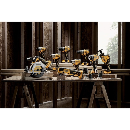 A collection of yellow and black DEWALT power tools arranged on a wooden workbench inside a construction site. The tools include drills, saws, and other cordless devices.