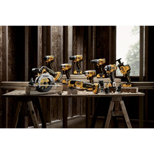 A collection of yellow and black DEWALT power tools displayed on wooden tables inside a construction area with unfinished walls.
