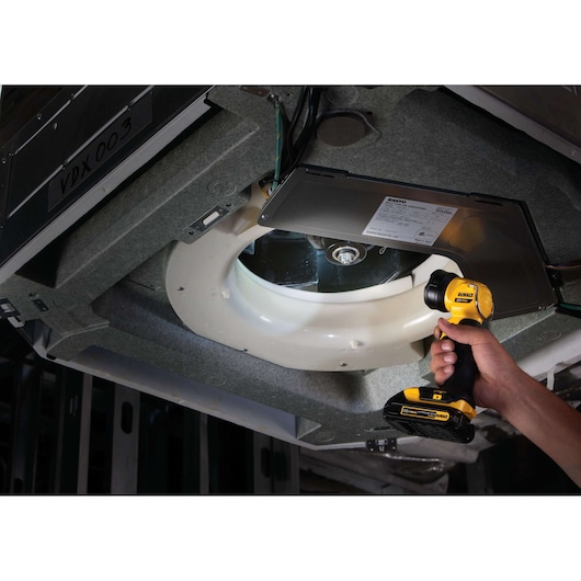 A person is using a DEWALT DCL040 handheld LED work light to illuminate a mechanical component in an industrial or maintenance setting.