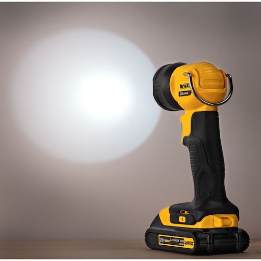 A DEWALT DCL040 portable LED work light with a 20V lithium-ion battery, shown turned on and projecting a bright beam onto a neutral background.
