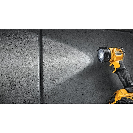 A yellow and black DEWALT handheld LED flashlight illuminating a textured gray wall.