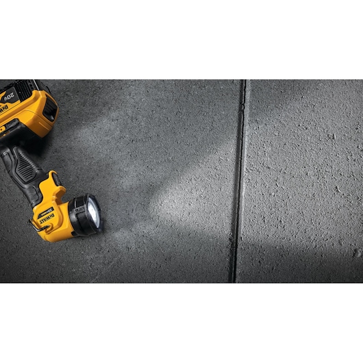 A yellow and black DEWALT portable LED flashlight is turned on and shining light onto a grey textured concrete surface.