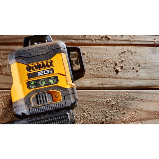 A close-up of a DEWALT 20V yellow and black laser level tool resting on a wooden surface covered with sawdust.