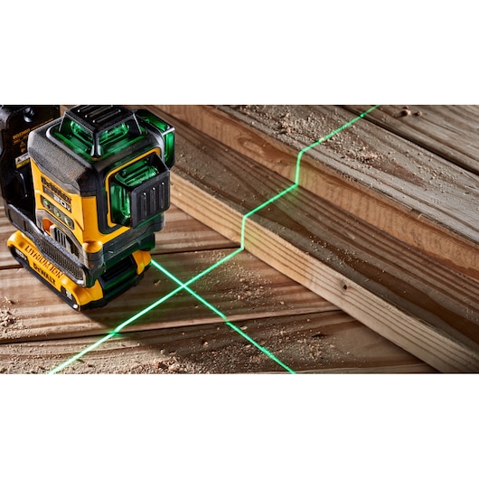 A DEWALT laser level tool projecting green cross lines onto wooden planks, used for precise alignment in construction or woodworking.
