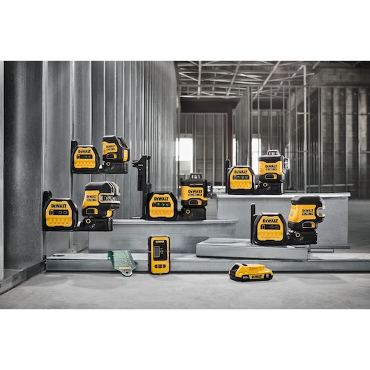 A collection of DEWALT yellow and black laser measuring tools and accessories displayed on metal steps in an unfinished industrial interior.