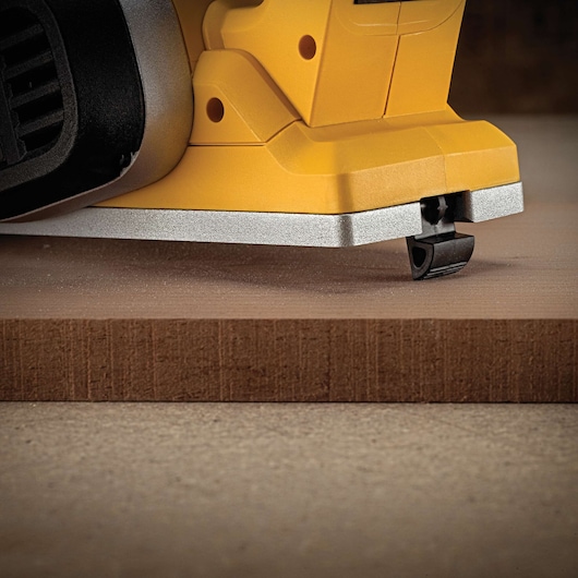 Close-up of a yellow DEWALT power tool with a metal base resting on a wooden surface.