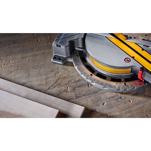 Close-up view of a DEWALT miter saw resting on a dusty workbench with two pieces of wood nearby.