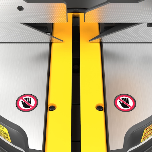 Close-up view of a DEWALT miter saw cutting area, showing metal cutting surfaces, a yellow central guide, and warning signs indicating to keep hands away from the blades.