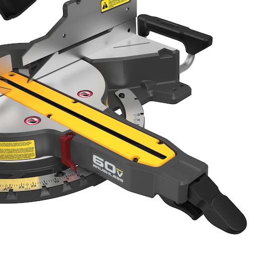 Close-up view of a DEWALT 60V MAX brushless miter saw, showing the blade, cutting platform, and handle. Visible safety and measurement markings are present on the tool.