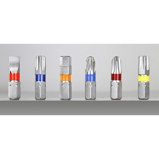 A row of six metallic screwdriver bits, each with a different tip shape and a colored band around the shank. The colors include red, blue, orange, and yellow. The bits are standing upright on a grey surface against a neutral background.