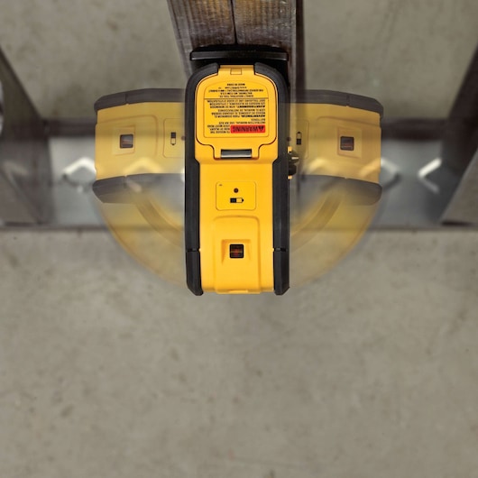 A yellow and black DEWALT laser level device mounted on a metal beam, viewed from above. The device's control panel and warning label are visible, with the image showing a motion effect to indicate its rotational capability.