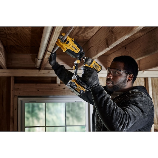 End user using DEWALT IMPACT CONNECT Copper Cutter attachment on Impact Driver to cut copper pipe running along board above his head.
