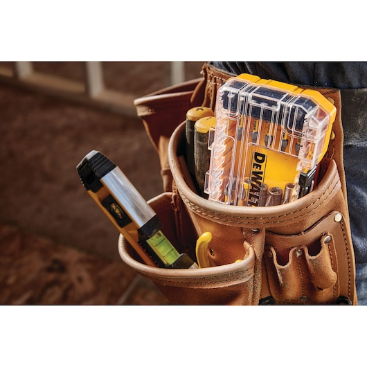 A close-up view of a brown leather tool belt containing various tools, including a clear plastic case holding DEWALT branded drill bits, a level, screwdrivers, and other hand tools.