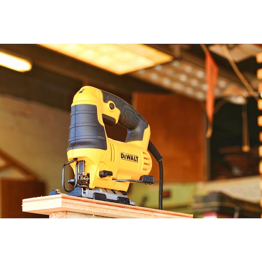 A yellow and black DEWALT jigsaw power tool placed on a piece of wood in a workshop setting.