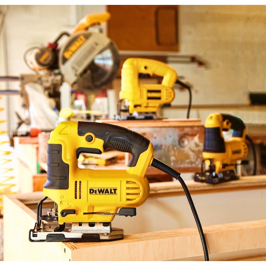 A close-up of a yellow DEWALT jigsaw power tool placed on a wooden surface, with other DEWALT tools visible in the background inside a workshop.