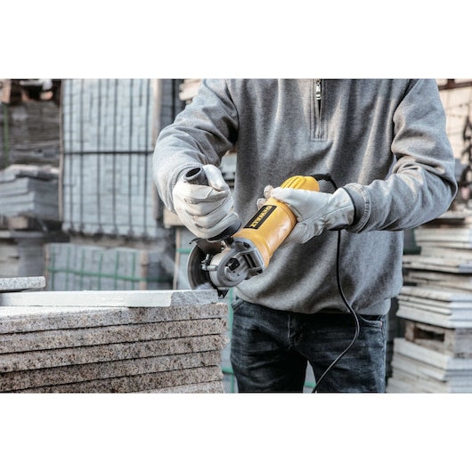 A person wearing gloves is using a yellow DEWALT DWE4010 angle grinder to cut stone slabs in an industrial setting.