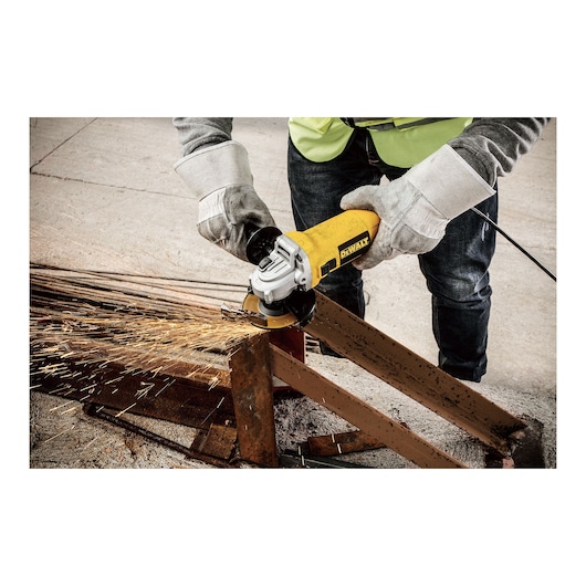 A person wearing protective gloves and a vest uses a DEWALT angle grinder (model DWE4010) to cut a metal beam, with sparks flying during the process.