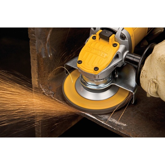 A close-up of a person using a yellow DEWALT angle grinder, producing sparks while grinding the edge of a metal surface. The individual is wearing protective gloves.