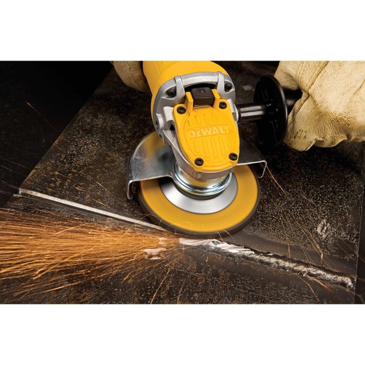 A DEWALT angle grinder being used to cut metal, with sparks flying from the cutting area. The worker is wearing protective gloves.